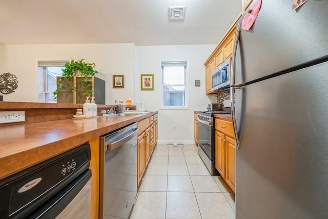 kitchen with wood counters, stainless steel appliances, sink, and light tile patterned floors