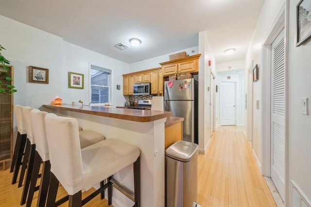 kitchen featuring backsplash, stainless steel appliances, a kitchen bar, kitchen peninsula, and light wood-type flooring