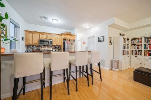 kitchen featuring light wood-type flooring, decorative backsplash, a breakfast bar area, and appliances with stainless steel finishes