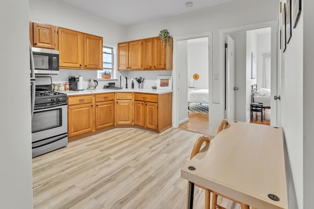 kitchen with stainless steel appliances, brown cabinets, light countertops, and light wood finished floors