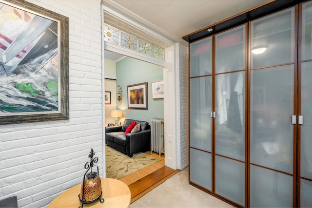 corridor featuring crown molding, brick wall, radiator, and light carpet