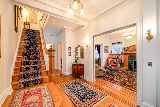 foyer with hardwood / wood-style floors, ornamental molding, a tile fireplace, and a chandelier