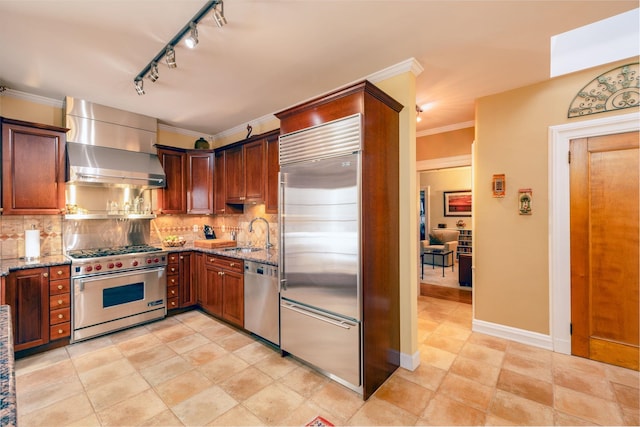 kitchen with sink, high end appliances, tasteful backsplash, light stone counters, and wall chimney range hood