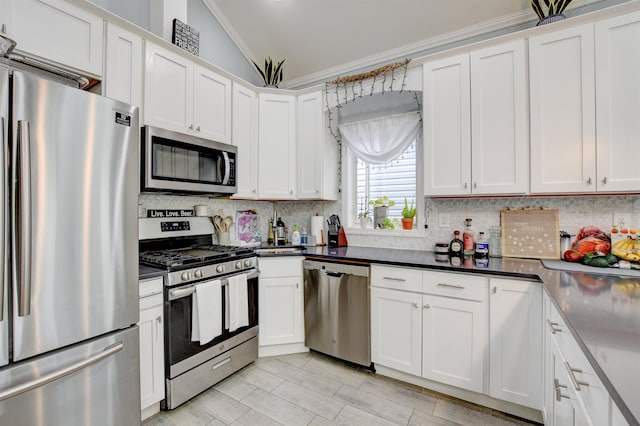 kitchen with white cabinets, crown molding, tasteful backsplash, appliances with stainless steel finishes, and vaulted ceiling