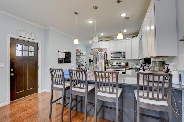 kitchen featuring backsplash, stainless steel appliances, ornamental molding, and light wood-type flooring