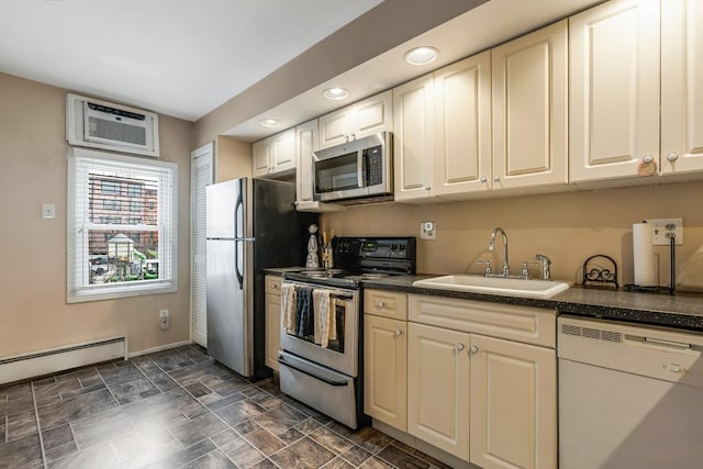 kitchen with dark countertops, appliances with stainless steel finishes, stone finish flooring, baseboard heating, and a sink