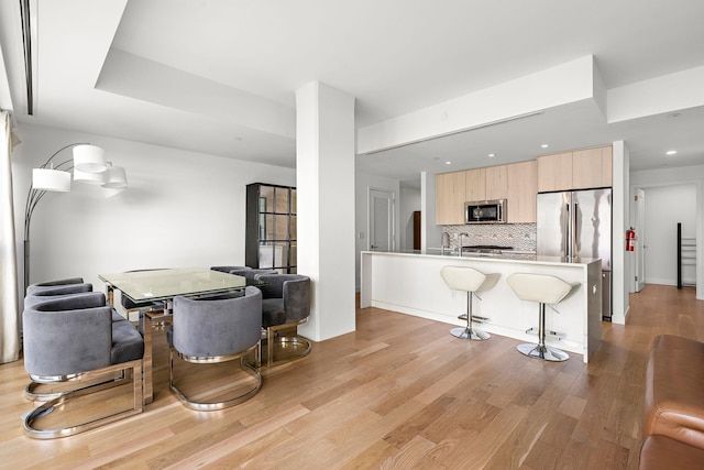 kitchen featuring a kitchen bar, appliances with stainless steel finishes, decorative backsplash, light brown cabinetry, and light hardwood / wood-style floors