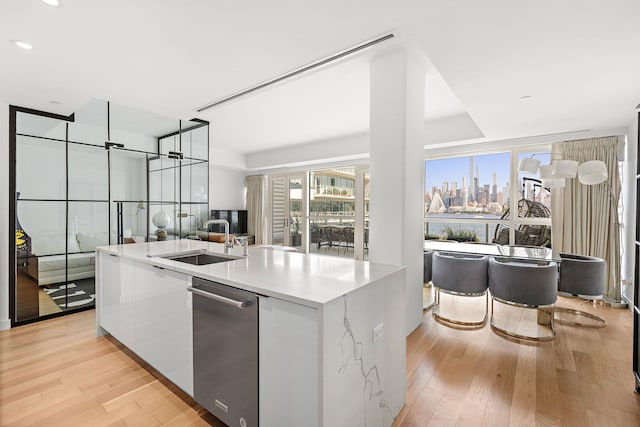 kitchen with white cabinetry, a center island with sink, light hardwood / wood-style floors, and sink