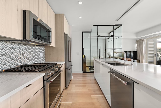 kitchen featuring sink, decorative backsplash, premium appliances, light hardwood / wood-style floors, and light stone counters