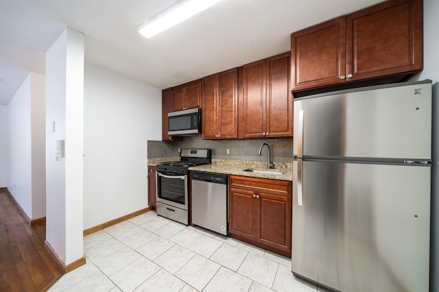 kitchen featuring a sink, light stone counters, backsplash, stainless steel appliances, and baseboards