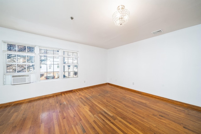 unfurnished room featuring visible vents, hardwood / wood-style floors, cooling unit, an inviting chandelier, and baseboards