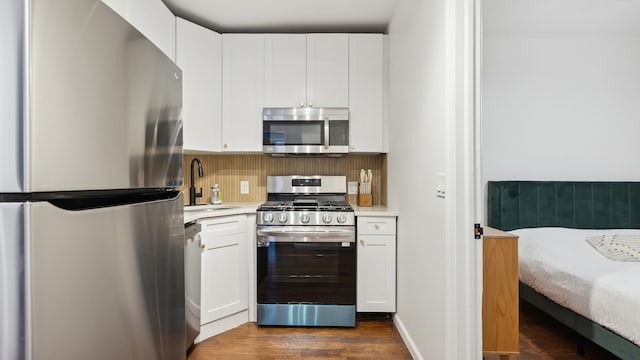 kitchen with appliances with stainless steel finishes, dark wood-type flooring, sink, white cabinetry, and backsplash