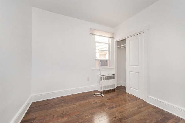 unfurnished bedroom with a closet, radiator heating unit, dark hardwood / wood-style flooring, and cooling unit