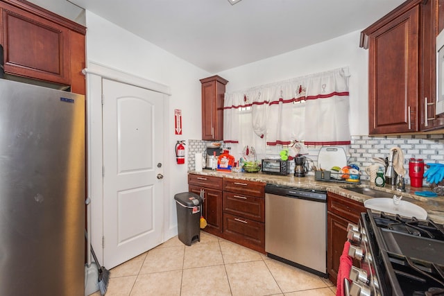 kitchen with appliances with stainless steel finishes, light tile patterned floors, backsplash, and light stone counters