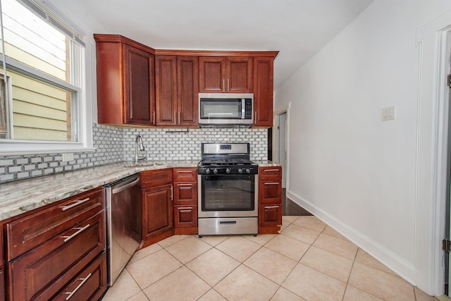 kitchen with light tile patterned flooring, appliances with stainless steel finishes, light stone counters, and decorative backsplash