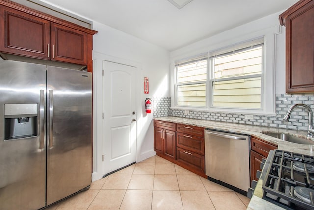 kitchen with light tile patterned flooring, appliances with stainless steel finishes, sink, backsplash, and light stone counters