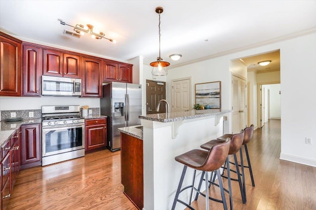 kitchen with reddish brown cabinets, a breakfast bar, stainless steel appliances, visible vents, and light wood-style flooring