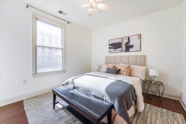 bedroom with a ceiling fan, visible vents, baseboards, and wood finished floors