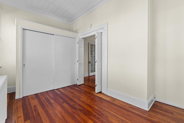 unfurnished bedroom featuring hardwood / wood-style floors, a closet, an ornate ceiling, and baseboards