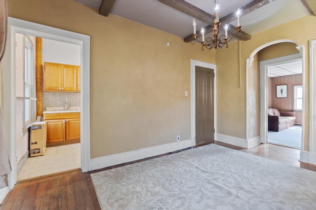 empty room with arched walkways, light wood-style floors, baseboards, beam ceiling, and a sink