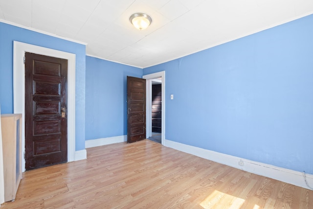 empty room featuring wood finished floors, ornamental molding, and baseboards