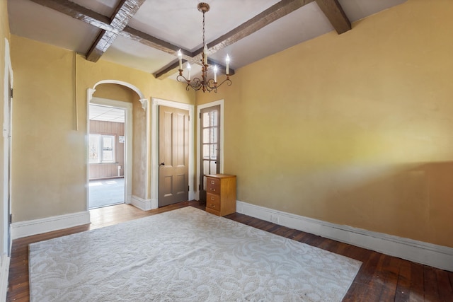 empty room with arched walkways, baseboards, hardwood / wood-style flooring, and beamed ceiling