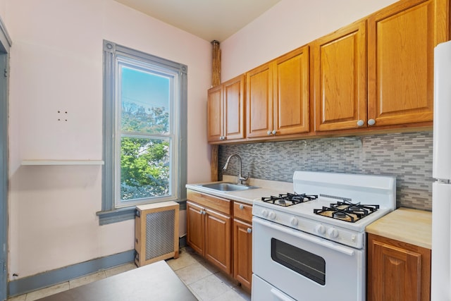 kitchen with white range with gas stovetop, a sink, backsplash, brown cabinetry, and light tile patterned floors