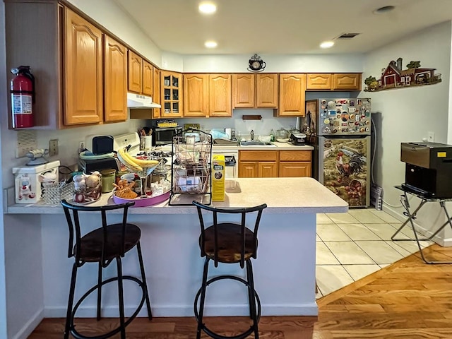 kitchen featuring black fridge, kitchen peninsula, sink, a kitchen breakfast bar, and light hardwood / wood-style flooring