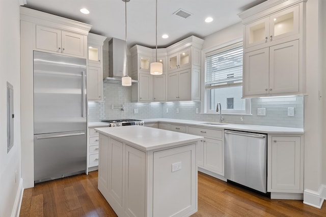 kitchen featuring appliances with stainless steel finishes, pendant lighting, a kitchen island, wall chimney exhaust hood, and white cabinets