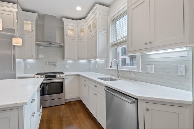 kitchen featuring stainless steel appliances, sink, white cabinetry, wall chimney exhaust hood, and hanging light fixtures