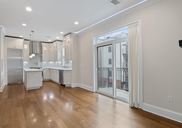 kitchen with wall chimney exhaust hood, pendant lighting, stainless steel appliances, decorative backsplash, and white cabinetry