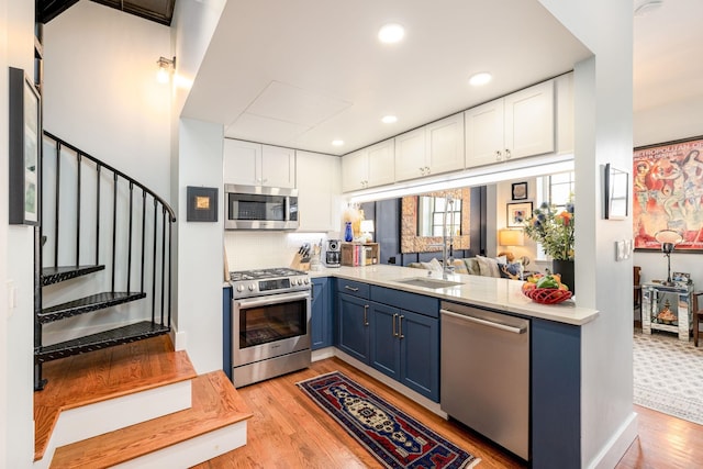 kitchen featuring light countertops, appliances with stainless steel finishes, white cabinetry, blue cabinets, and a sink