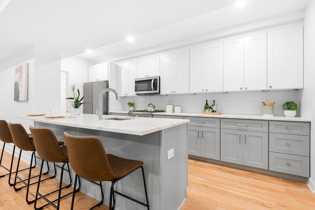 kitchen with a center island with sink, gray cabinetry, light hardwood / wood-style flooring, and appliances with stainless steel finishes