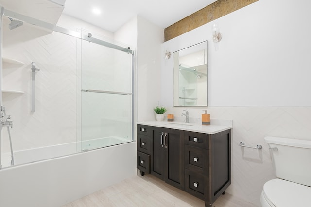 full bathroom featuring shower / bath combination with glass door, vanity, toilet, and tile walls