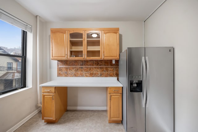 kitchen featuring backsplash, stainless steel fridge, light countertops, glass insert cabinets, and baseboards