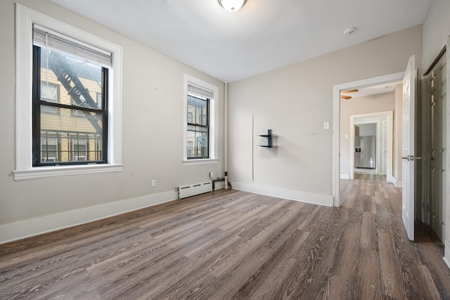 unfurnished room featuring a baseboard heating unit, baseboards, a healthy amount of sunlight, and wood finished floors