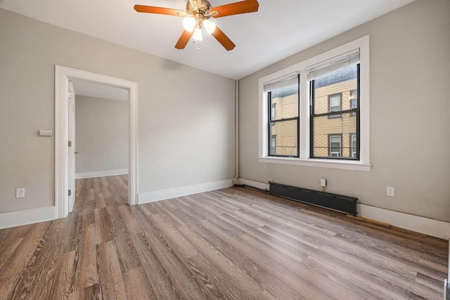 spare room featuring a baseboard radiator, a ceiling fan, baseboards, and wood finished floors