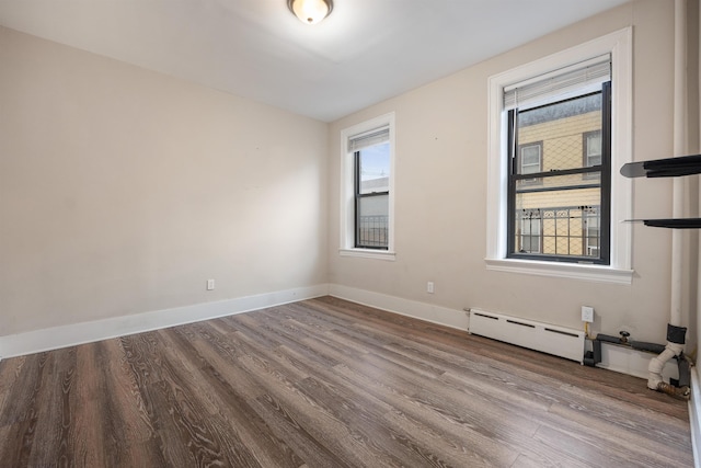 unfurnished room with a baseboard heating unit, wood finished floors, and baseboards