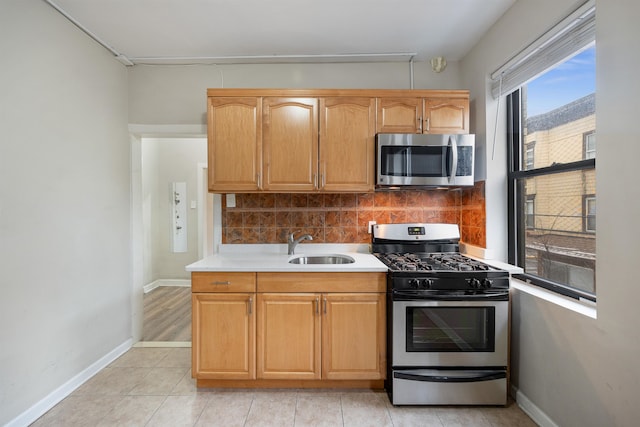 kitchen with a sink, backsplash, appliances with stainless steel finishes, light countertops, and baseboards