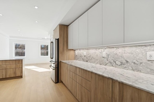 kitchen with tasteful backsplash, stainless steel fridge, white cabinets, light hardwood / wood-style floors, and light stone countertops