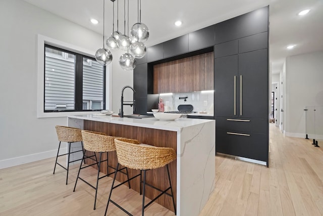 kitchen featuring a breakfast bar area, an island with sink, sink, light hardwood / wood-style flooring, and decorative light fixtures