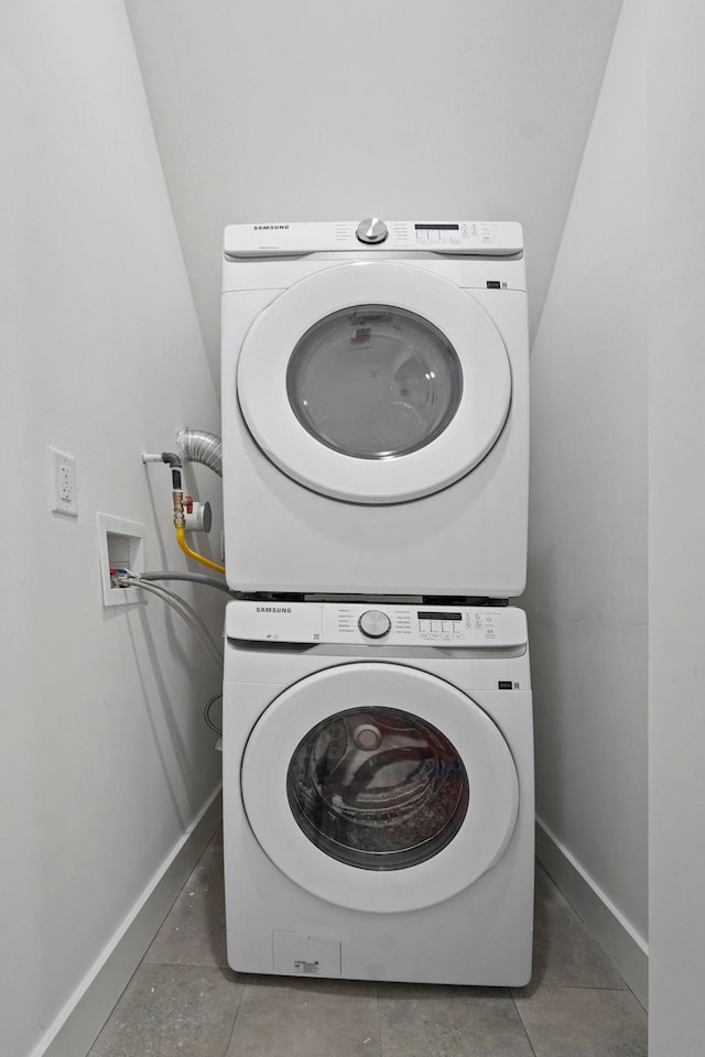 laundry room with dark tile patterned floors and stacked washer / dryer