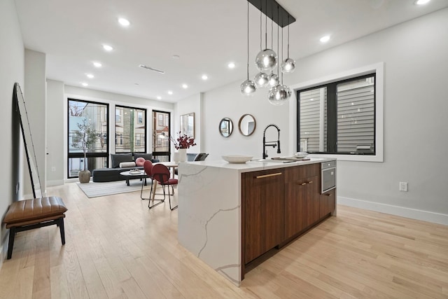 kitchen with light stone countertops, light hardwood / wood-style flooring, decorative light fixtures, a kitchen island with sink, and sink