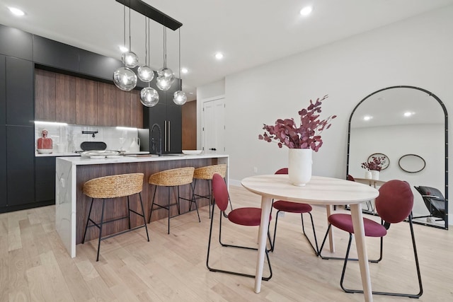 kitchen with sink, light hardwood / wood-style floors, tasteful backsplash, hanging light fixtures, and a kitchen island with sink