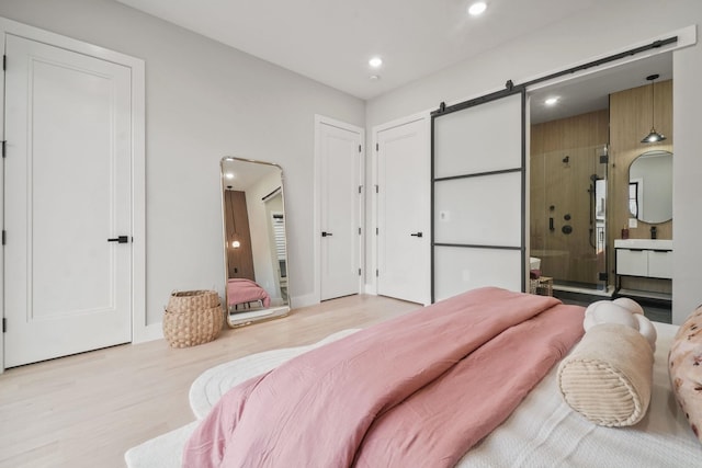 bedroom featuring ensuite bath, light wood-type flooring, and a barn door