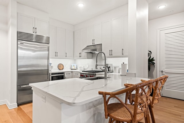 kitchen with white cabinetry, kitchen peninsula, stainless steel appliances, light stone countertops, and light hardwood / wood-style floors