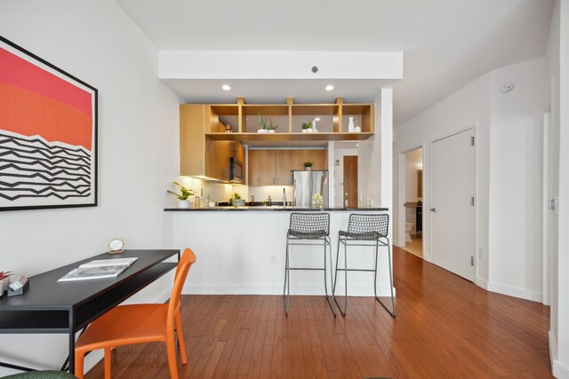 kitchen with a peninsula, freestanding refrigerator, open shelves, dark countertops, and wood finished floors