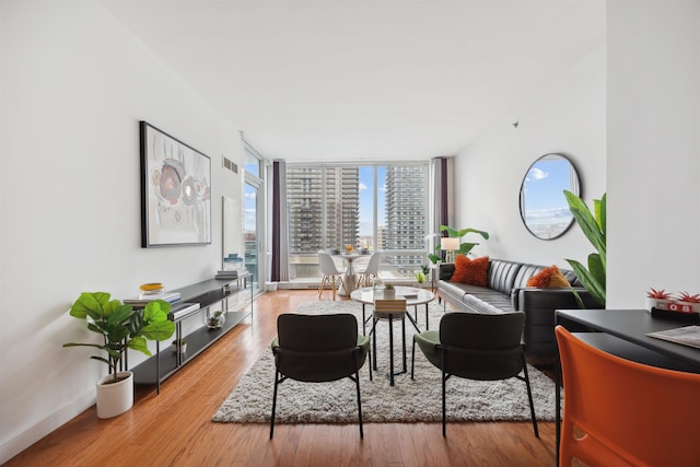 living room with visible vents, baseboards, a view of city, a wall of windows, and wood finished floors