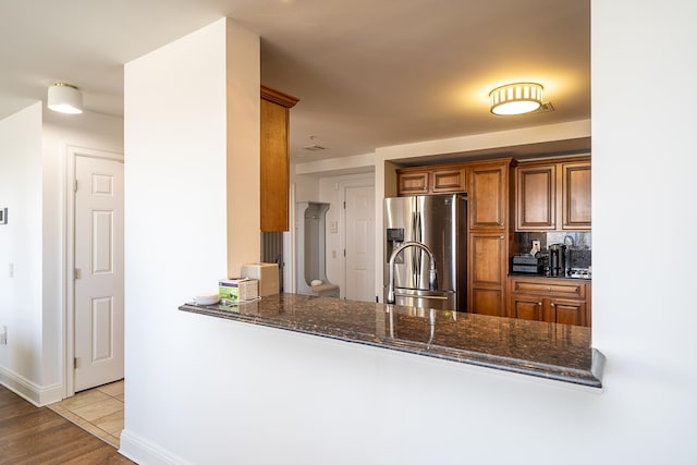 45 Broadway Unit 302, Jersey City, NJ 07306 - kitchen with stainless steel fridge with ice dispenser, dark stone counters, brown cabinetry, decorative backsplash, and a peninsula