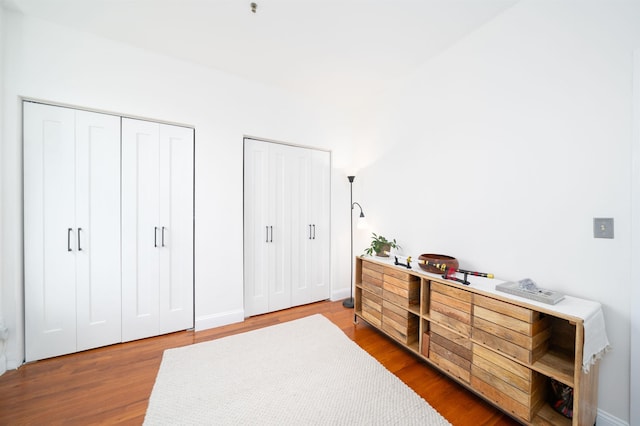 bedroom with baseboards, multiple closets, and wood finished floors